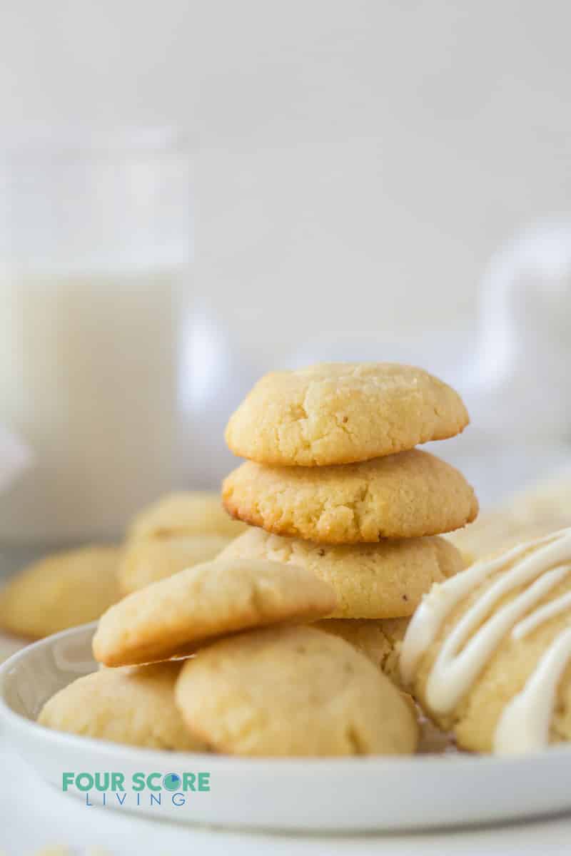 a stack of cream cheese cookies on a plate next to a glass of milk.