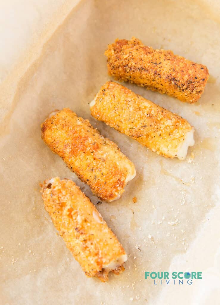 baked mozzarella sticks on a parchment lined tray.