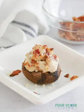 A cheesy stuffed mushroom with bacon on a small square plate.