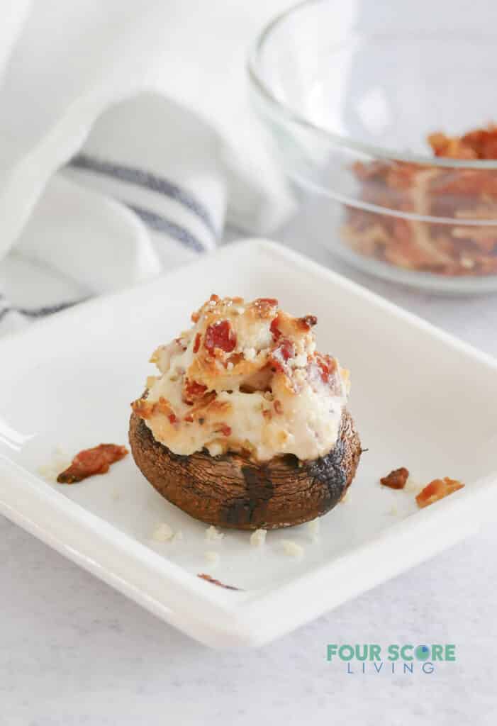 A cheesy stuffed mushroom with bacon on a small square plate.