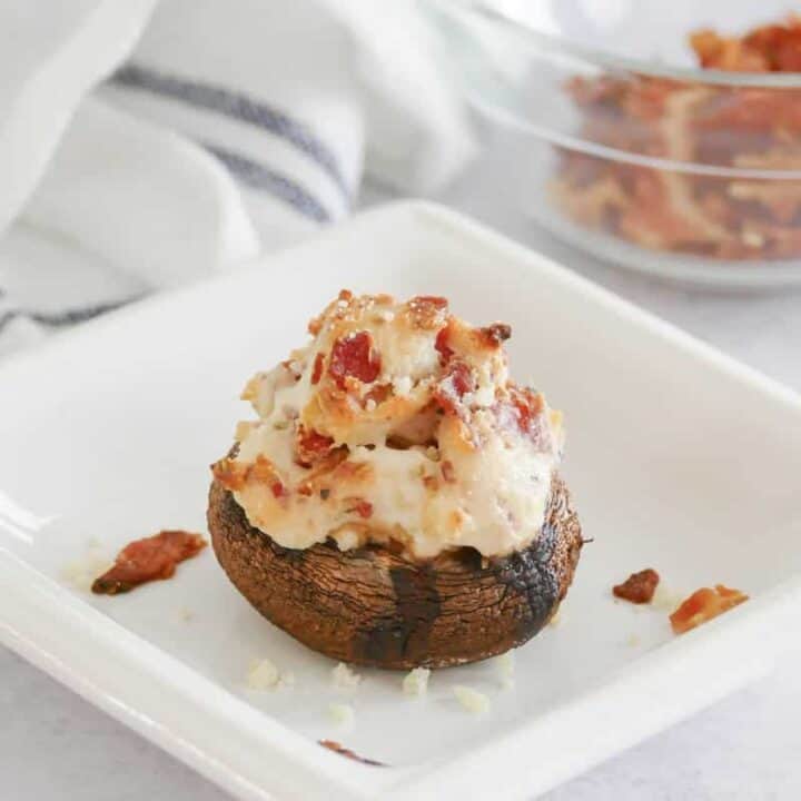 A cheesy stuffed mushroom with bacon on a small square plate.