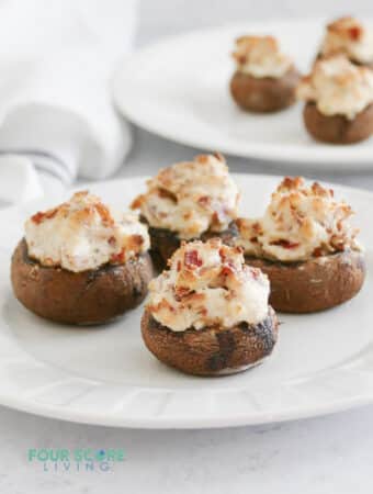 A round white plate of stuffed mushrooms filled with bacon and cheese.