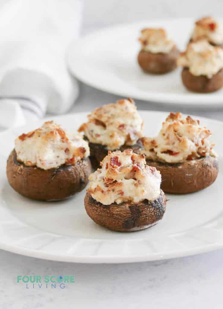 A round white plate of stuffed mushrooms filled with bacon and cheese.