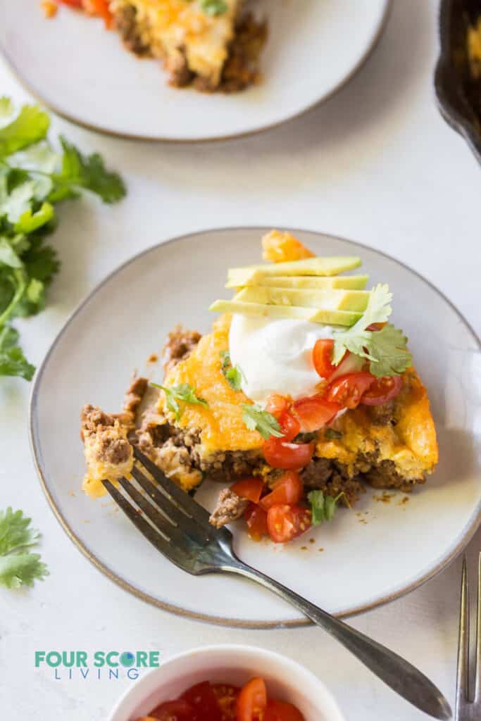 a slice of taco pie on a plate, topped with sour cream, avocoado, tomatoes, and cilantro.