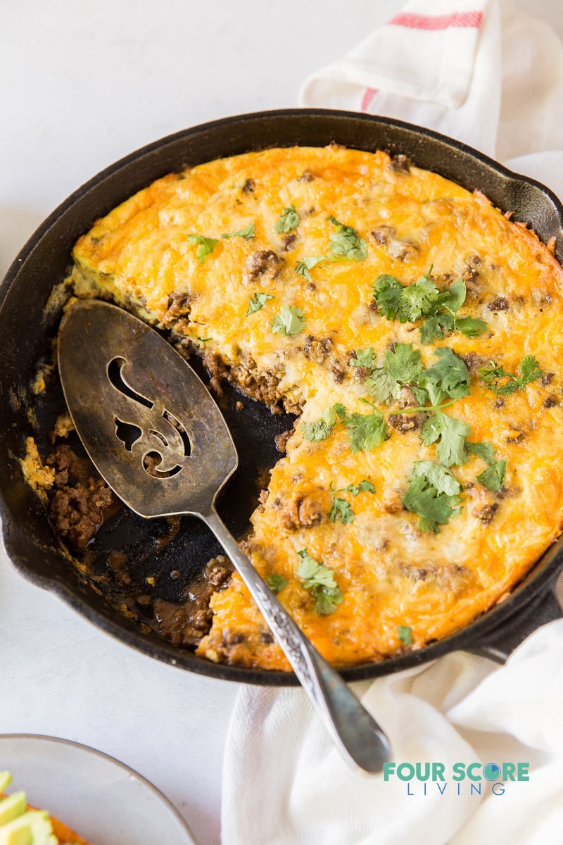 Taco pie in a cast iron skillet with two slices gone. 