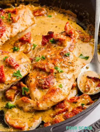 a cast iron skillet filled with chicken in a creamy sauce toped with sundried tomatoes and parsley.