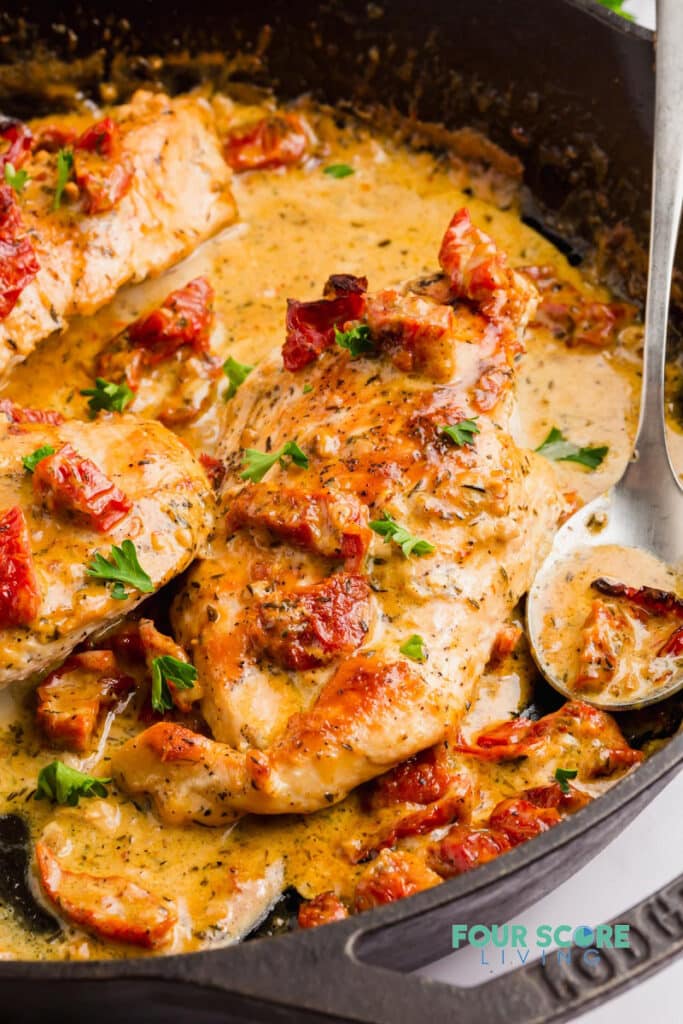 A cast iron skillet filled with chicken in a creamy sauce toped with sundried tomatoes and parsley.