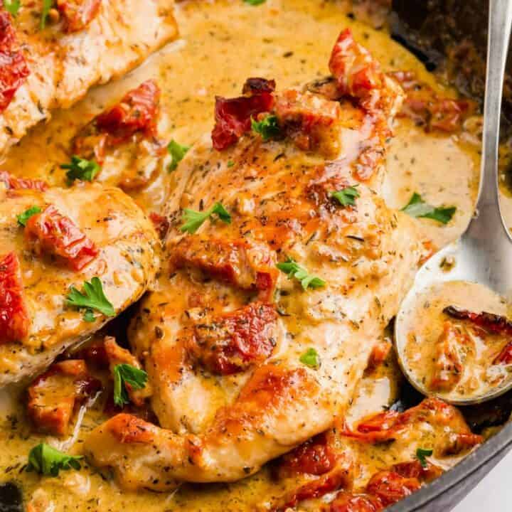 a cast iron skillet filled with chicken in a creamy sauce toped with sundried tomatoes and parsley.