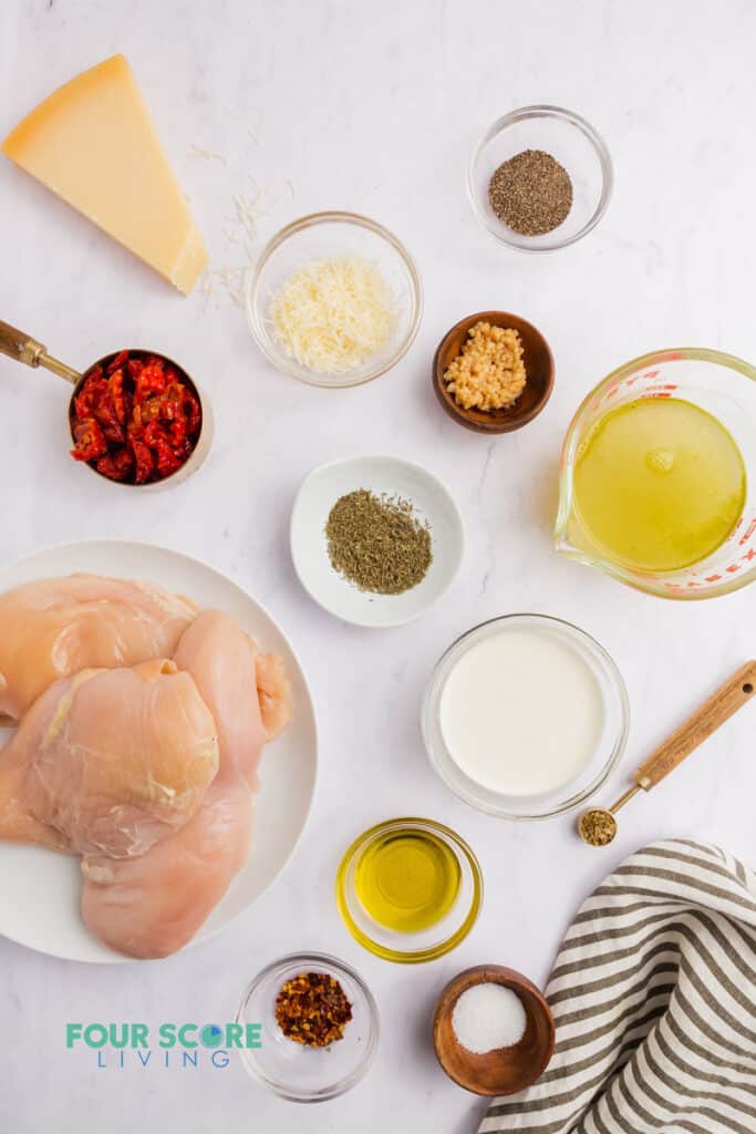 Ingredients for marry me chicken in separate bowls, including chicken, spices, sundried tomatoes, and parmesan cheese.