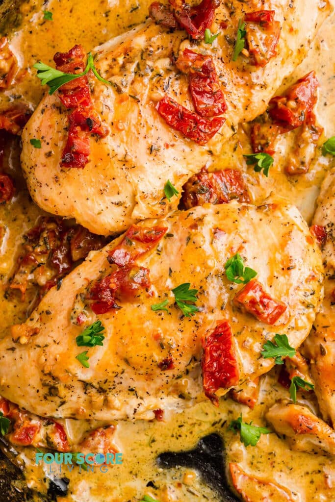 Closeup of marry me chicken. chicken breasts in a creamy sauce topped with sundried tomatoes and parsley.