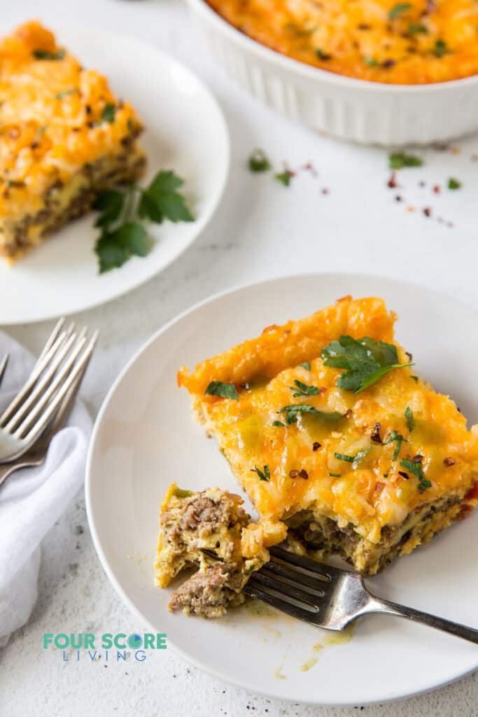 a square of breakfast casserole on a plate being eaten with a fork