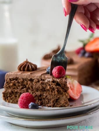 a slice of chocolate cake being eaten with a fork held by a feminine hand with red nail polish.