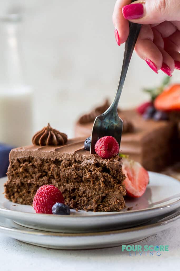 a slice of chocolate cake being eaten with a fork held by a feminine hand with red nail polish.