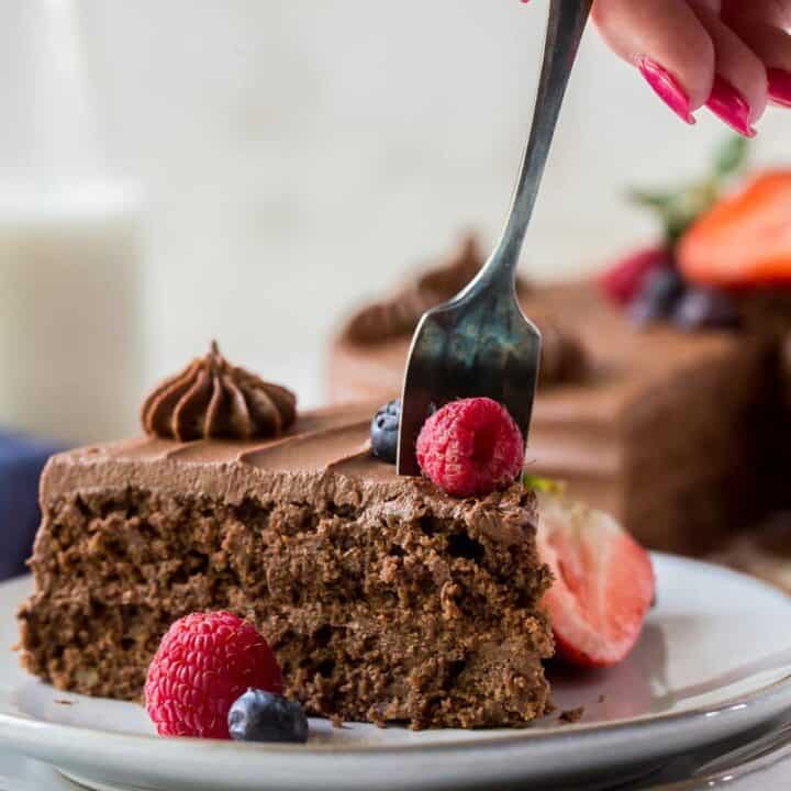 a slice of chocolate cake being eaten with a fork held by a feminine hand with red nail polish.