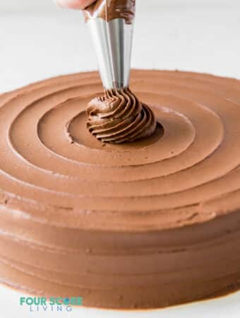 A chocolate cake being decorated with a piping bag in a swirl pattern.