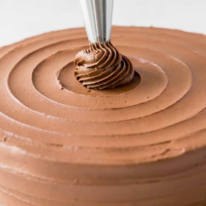 A chocolate cake being decorated with a piping bag in a swirl pattern.