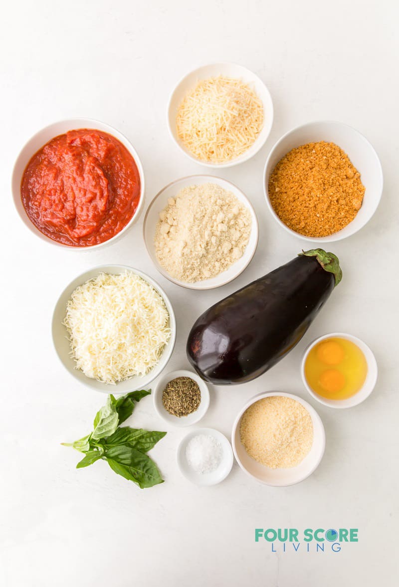 top down view of ingredients for eggplant parmesan, including sauce, seasonings, cheeses, eggplant, and eggs.