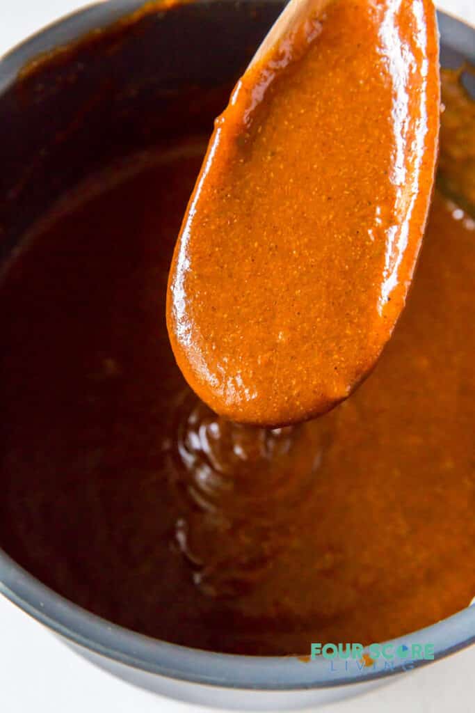 A pot of enchilada sauce being stirred with a wooden spoon.
