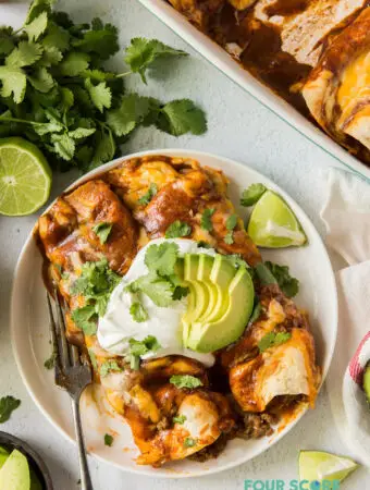 two enchiladas on a plate topped with sour cream, avocado, and cilantro.
