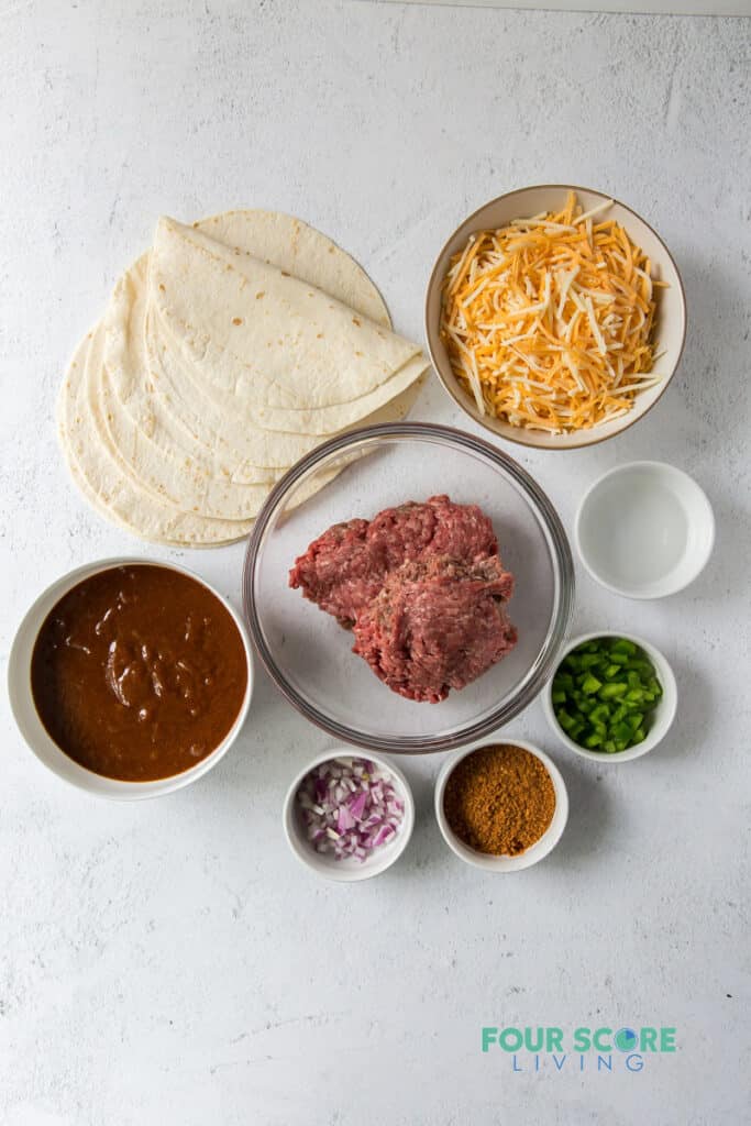 top down view of ingredients for keto enchiladas, including tortillas, cheese, meat, sauce, and seasonings.