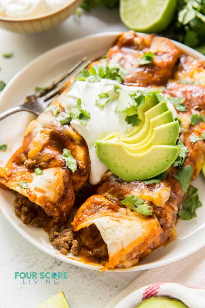 Closeup view of two enchiladas on a plate topped with sour cream, avocado, and cilantro.