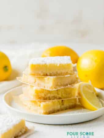 a plate of 4 lemon bars, stacked on top of each other, surrounded by lemons.