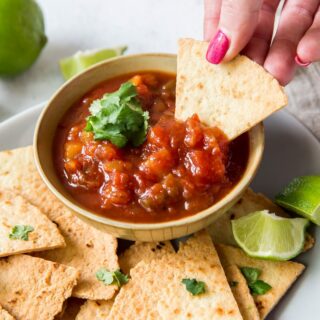 a bowl of salsa and homemade tortilla chips. A woman is dipping a chip into the salsa.