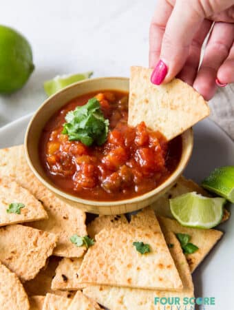 a bowl of salsa and homemade tortilla chips. A woman is dipping a chip into the salsa.