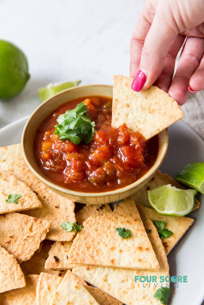a bowl of salsa and homemade tortilla chips. A woman is dipping a chip into the salsa.