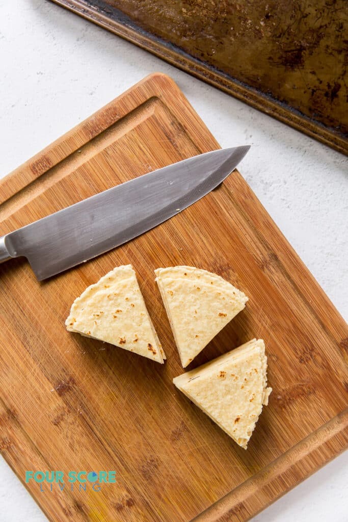 a wooden cutting board with tortilla triangles and a large knife on it.