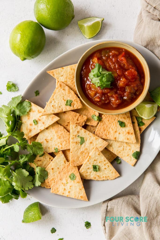 a tray of chips and salsa garnished with lime wedges and cilantro.