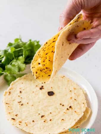 A hand folding a tortilla over a plate of tortillas.