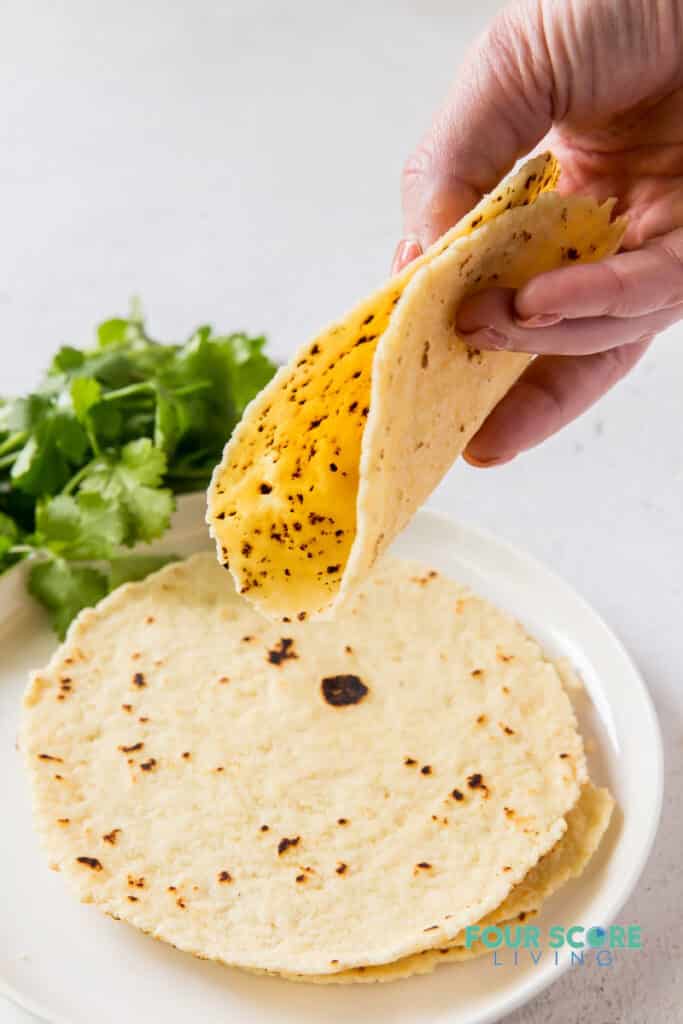 A hand folding a tortilla over a plate of tortillas.
