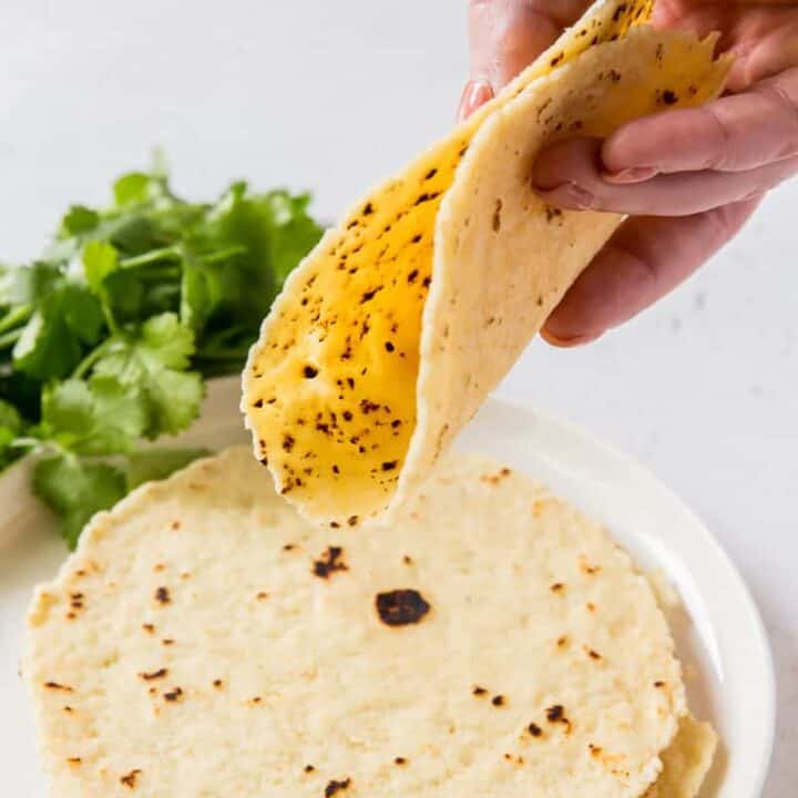 A hand folding a tortilla over a plate of tortillas.