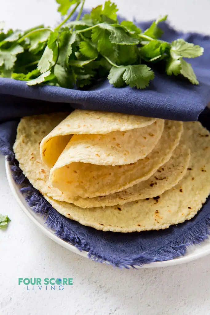 a plate of tortillas wrapped in a blue towel with a cilantro garnish.