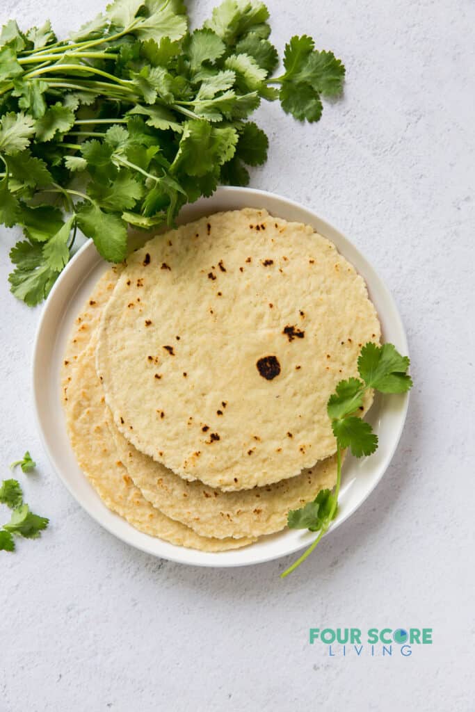 top down view of a plate of tortillas next to a bunch of cilantro.