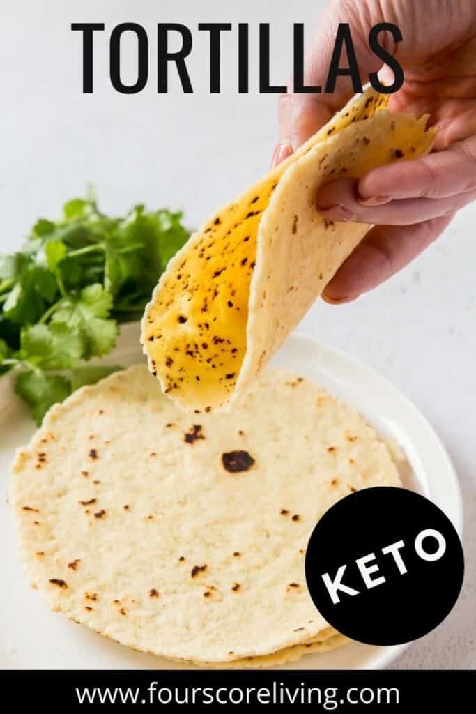a hand holding a tortilla over a plate of tortillas.