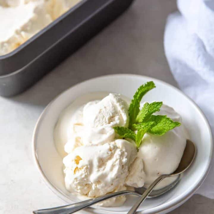a bowl of vanilla ice cream with mint garnish and two spoons