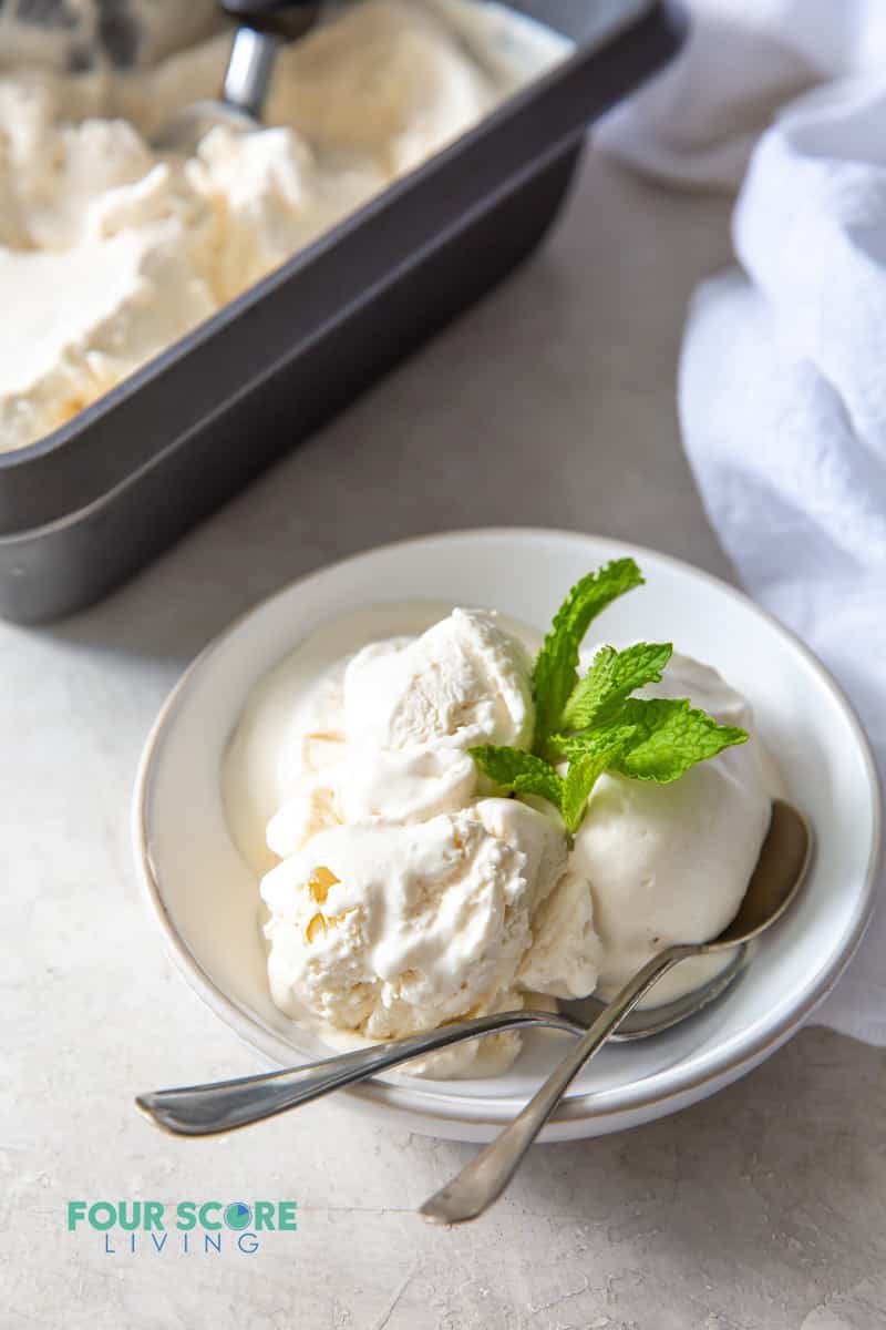 a bowl of vanilla ice cream with mint garnish and two spoons