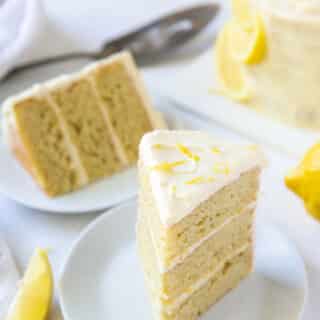 Two plates each with a three layer slice of lemon cake.