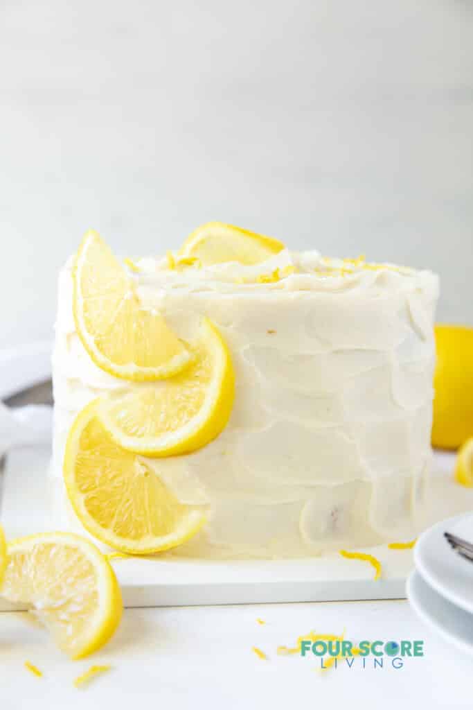 a round, tall cake with white frosting and garnished with lemon slices.