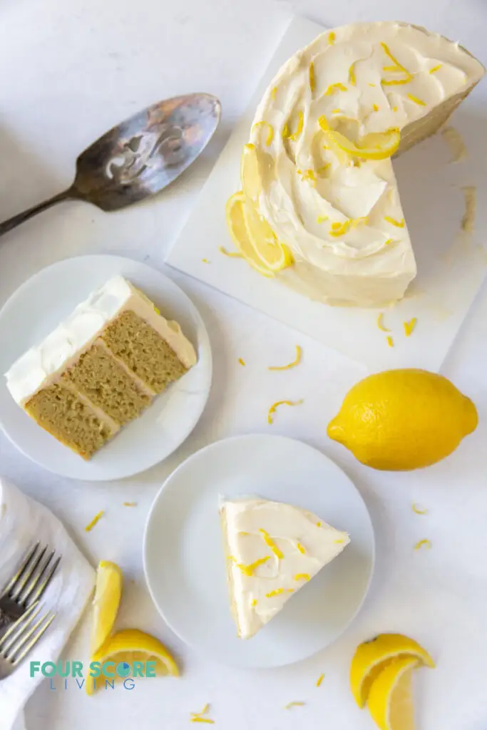 top down view of a lemon cake being served, and two plated slices of cake. Lemons and lemon slices garnish the cake.