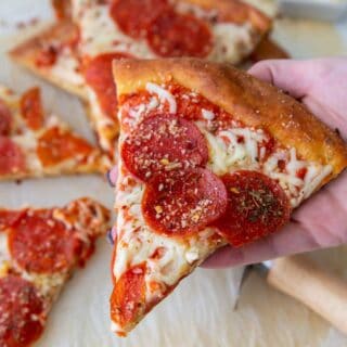 a hand picking up a slice of pepperoni pizza topped with herbs.
