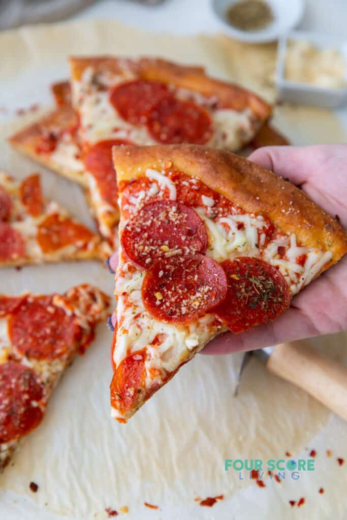 a hand picking up a slice of pepperoni pizza topped with herbs.