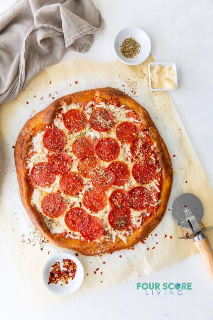 top down view of a pepperoni pizza on a piece of parchment paper garnished with herbs and cheese