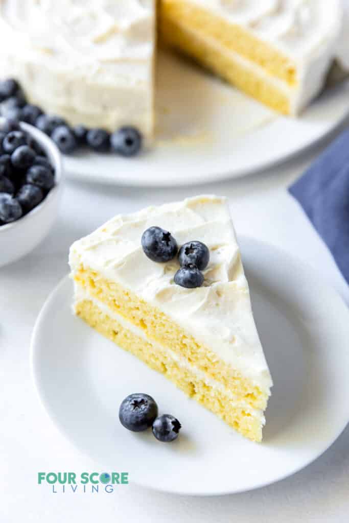 a slice of vanilla layer cake on a white plate, topped with blueberries.