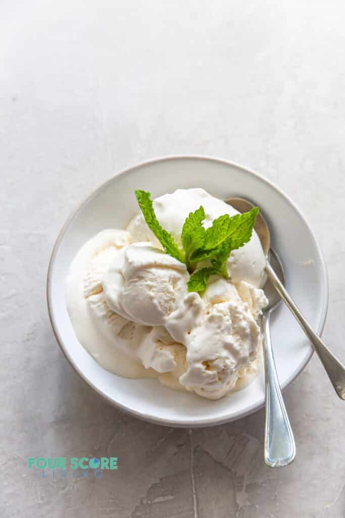 a white bowl of vanilla ice cream topped with fresh mint with two spoons.