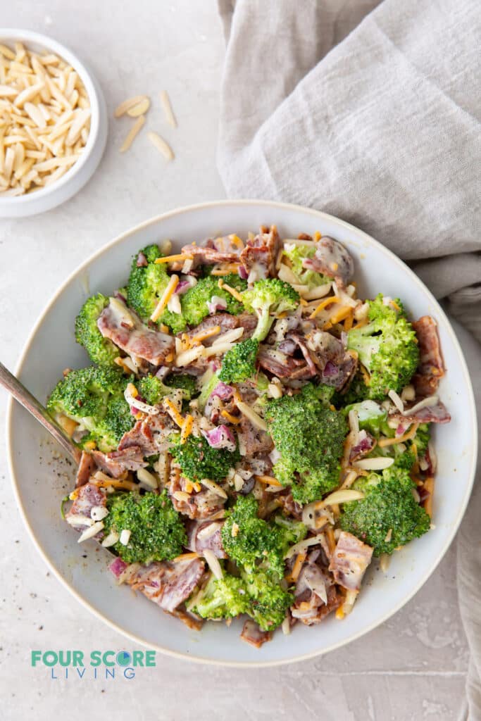 a large white bowl filled with broccoli salad with cheese and bacon