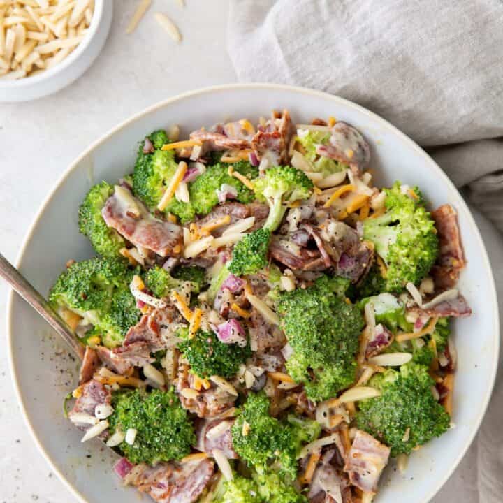 a large white bowl filled with broccoli salad with cheese and bacon