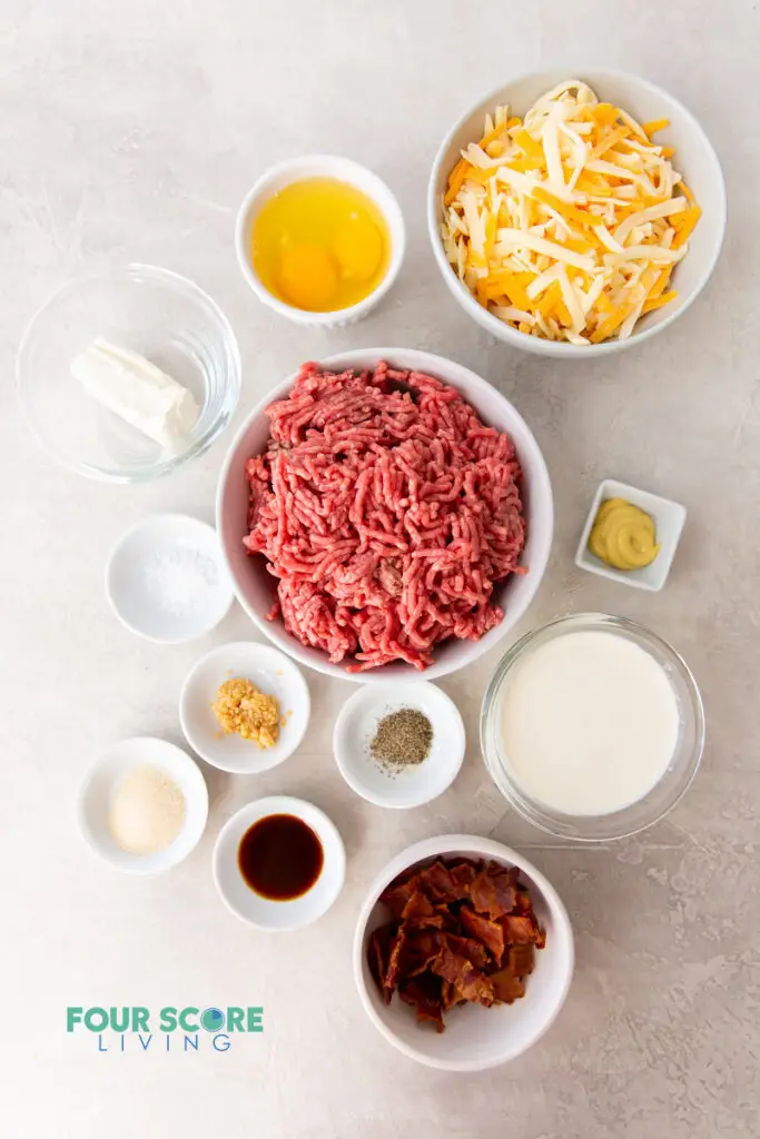 top down view of the ingredients needed for cheeseburger casserole, all in separate dishes. Includes hamburger meat, cheese, eggs, bacon, and seasonings